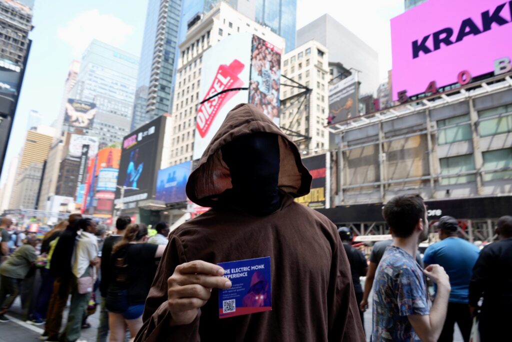 man in monk robes in times square holding up a flyter to monks