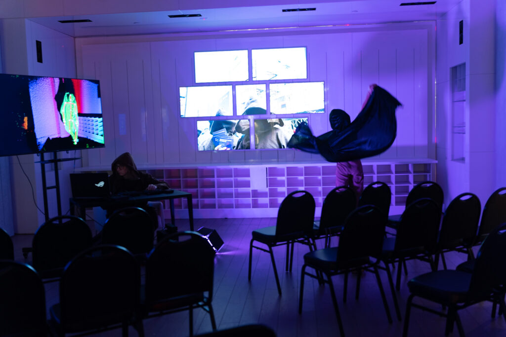 gallery with 7 artfully arranged video monitors and a man in monk robes flailing his robe