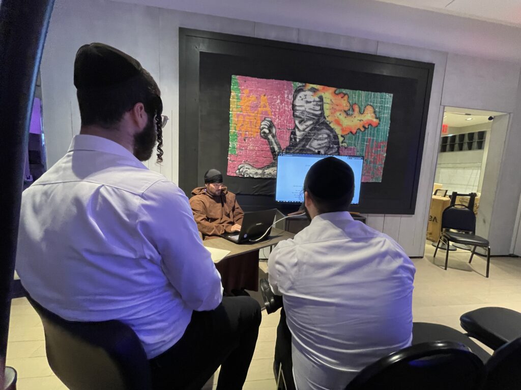 two jewish people with yamakas listing to a man in a monk robe in front of a tv